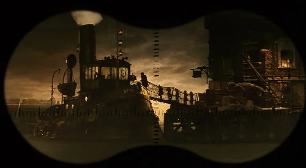 The City Of Lost Children movie still: wide — A dark industrial wharf at night is seen through the circular view of binoculars. Small silhouettes of…
