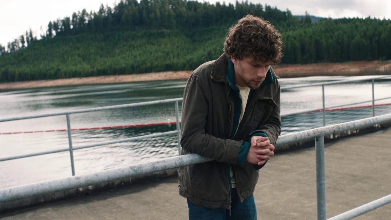 Night Moves (2013) movie still: medium — A man stands on a concrete dock next to a calm lake bordered by evergreen trees. The man leans forward with…