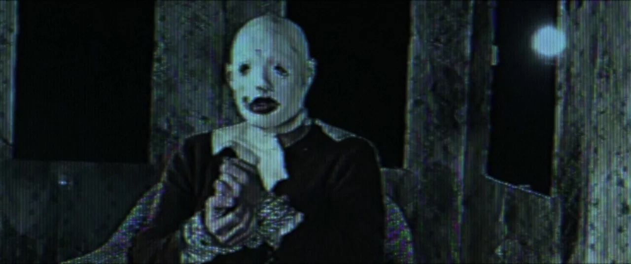Broadcast Signal Intrusion (2021) movie still: medium — A dark carriage interior features a textured wall and a small glowing light. A bald figure…