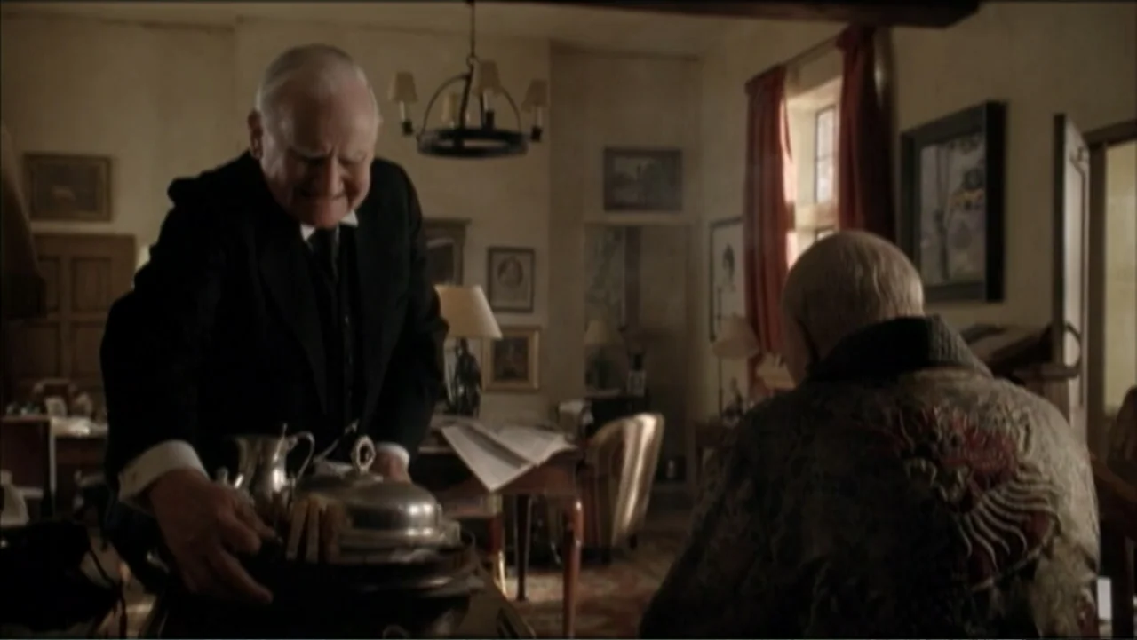 The Gathering Storm (2002) movie still: medium — A cluttered 1940s study contains a wooden desk, table lamps, and dark patterned rugs. A man in a…