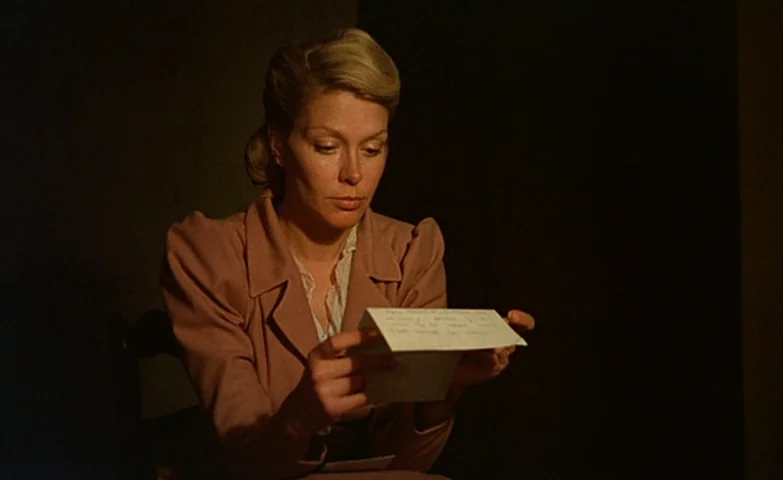 Spirit Of The Beehive (1973) movie still: medium — A woman sits in a dark, indistinct room against a plain black background. She holds a white piece…