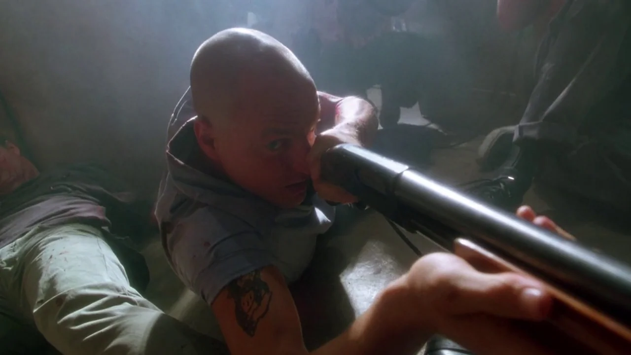 Natural Born Killers (1994) movie still: closeup — A dimly lit, hazy interior space filled with thick particulate matter. A bald man aims a shotgun…
