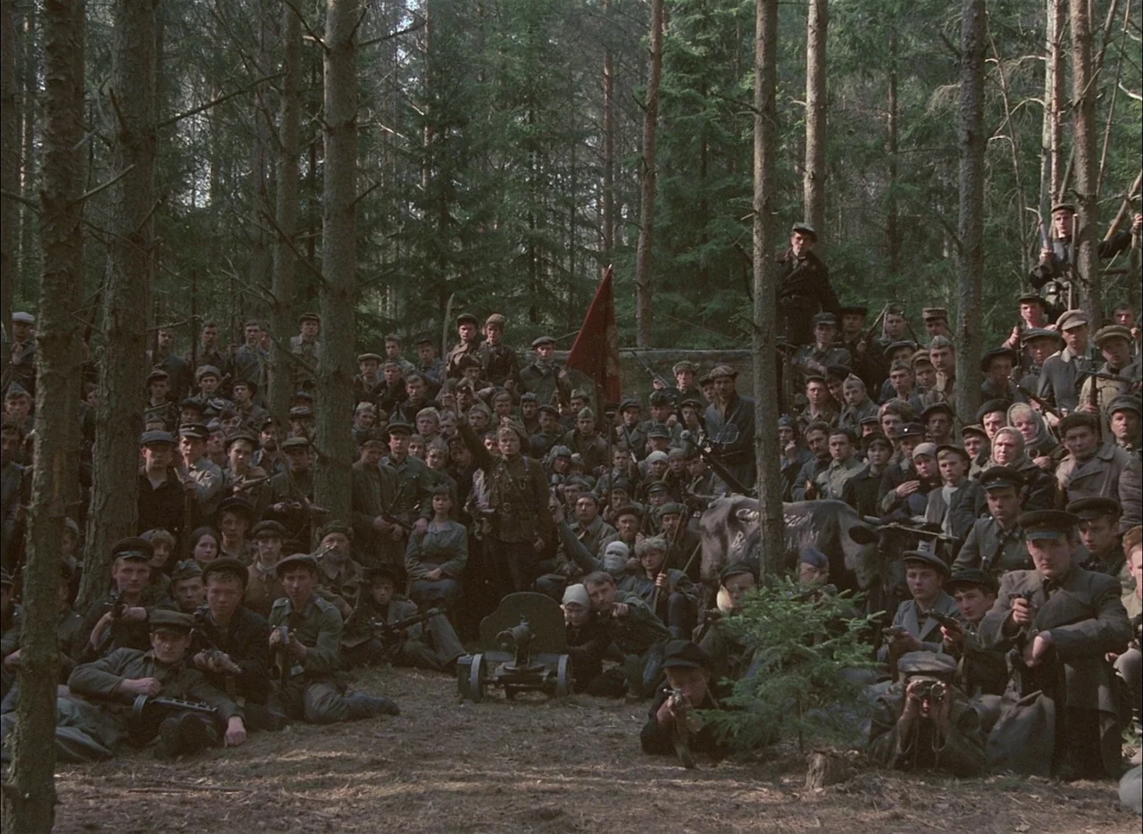 Come and See (1985) movie still: wide — A dense coniferous forest contains a large, assembled group of armed partisans and soldiers. The subjects…