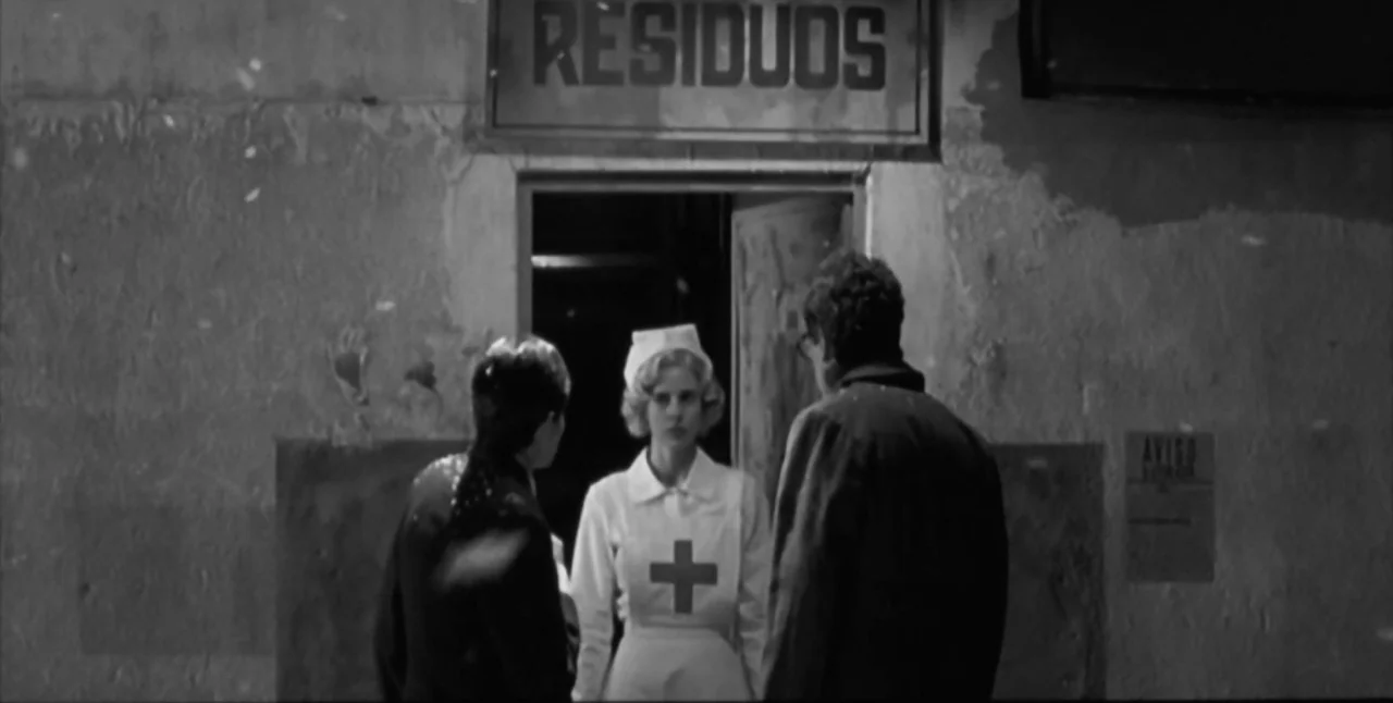 The Aerial (2007) movie still: fullbody — A dark outdoor setting features a doorway marked by a sign reading RESIDUOS. Three individuals interact…