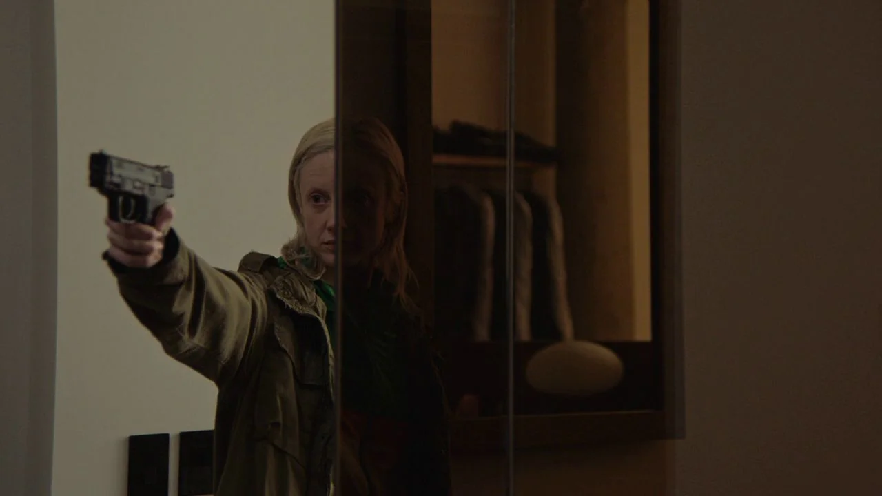 Possessor (2020) movie still: medium — A dark, modern interior features a woman partially reflected in a mirrored wardrobe door. She points a…