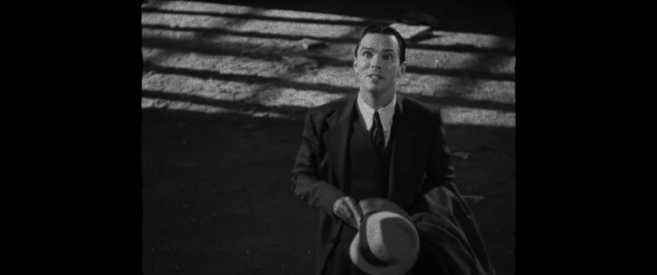 Renfield (2023) movie still: medium — A dark city street at night features strong light casting long shadows across pavement. A young man in a…