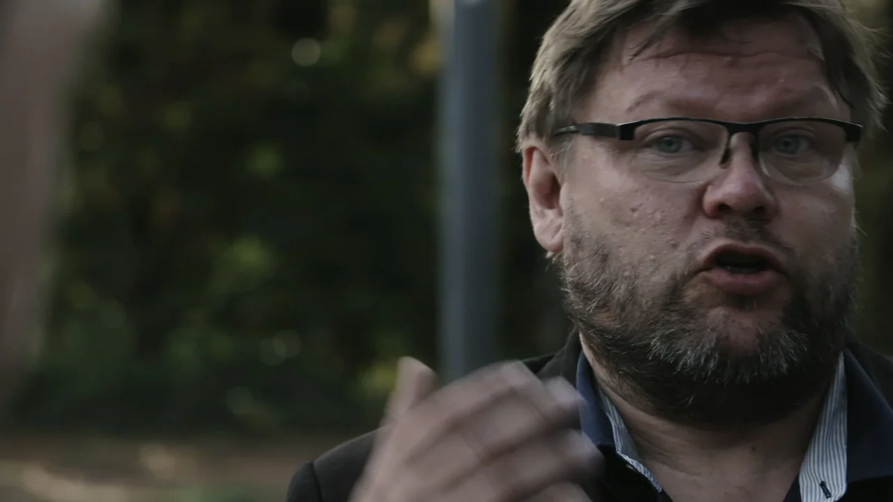 Kill Chain: The Cyber War on America's Elections (2020) movie still: closeup — An outdoor park setting with blurred greenery in the background. A…