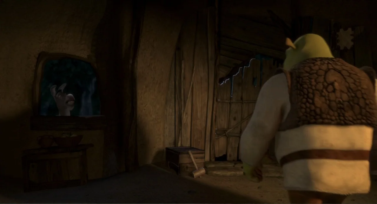 Shrek (2001) movie still: medium — The interior of a rustic mud-walled structure features wooden doors and a small window. A green-skinned humanoid…