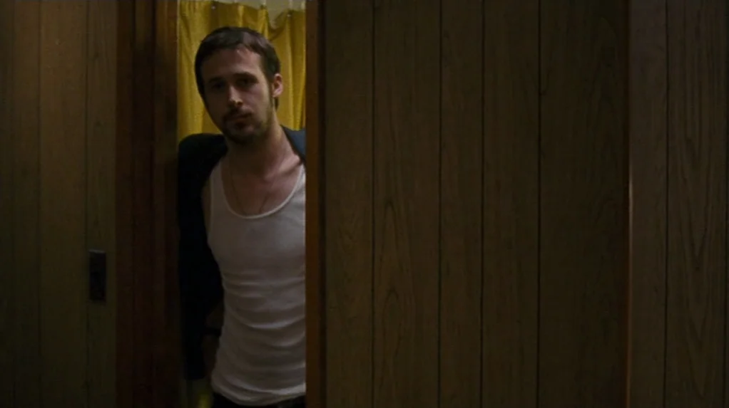 Half Nelson (2006) movie still: medium — A dimly lit room with vertical wood paneling and a yellow fabric partition. A man in an undershirt stands…