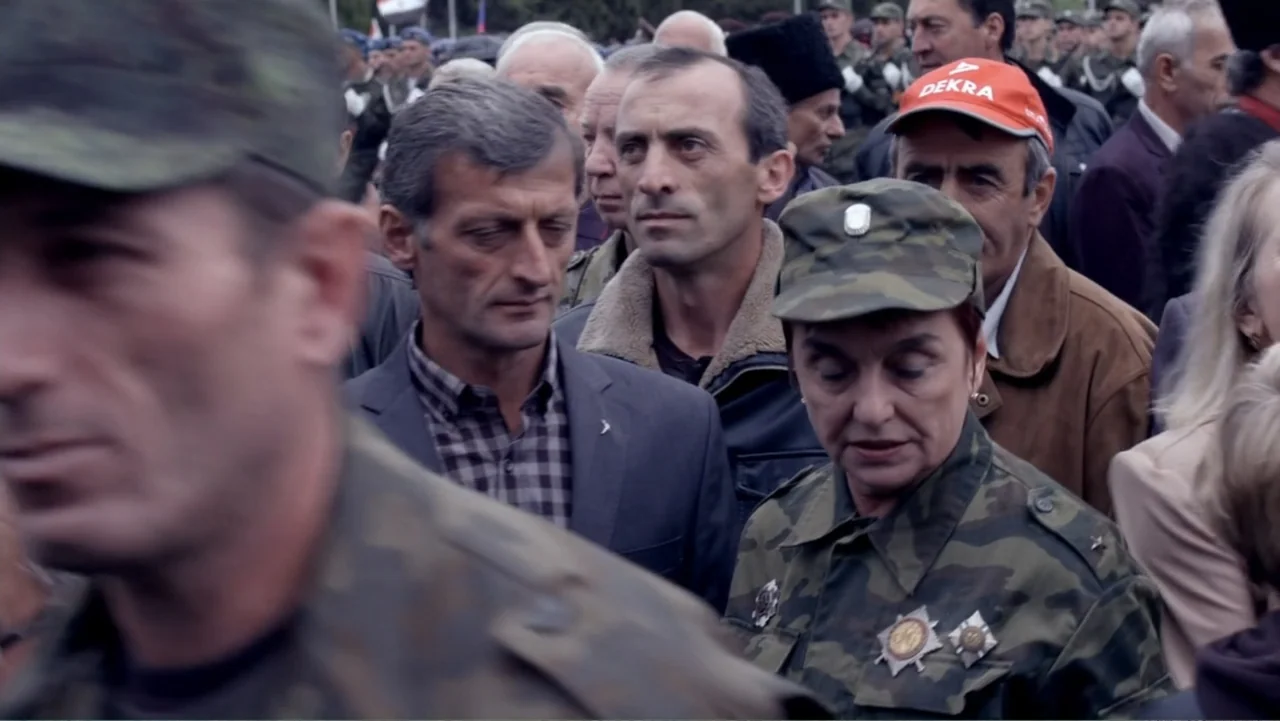 Letters to Max (2014) movie still: medium — An outdoor gathering of people in military and civilian attire during daytime. The subjects stand…