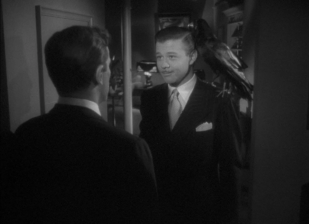The Amazing Mr. X (1948) movie still: medium — A dimly lit indoor space featuring two men in formal suits facing each other. The man on the right…