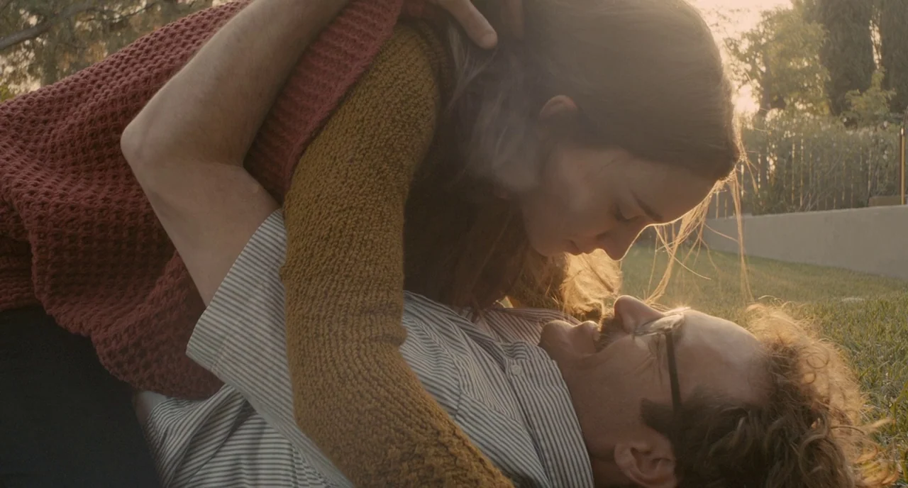 Her (2013) movie still: medium — A sun-drenched grassy yard serves as the backdrop during a warm afternoon. A woman and a man are lying close…