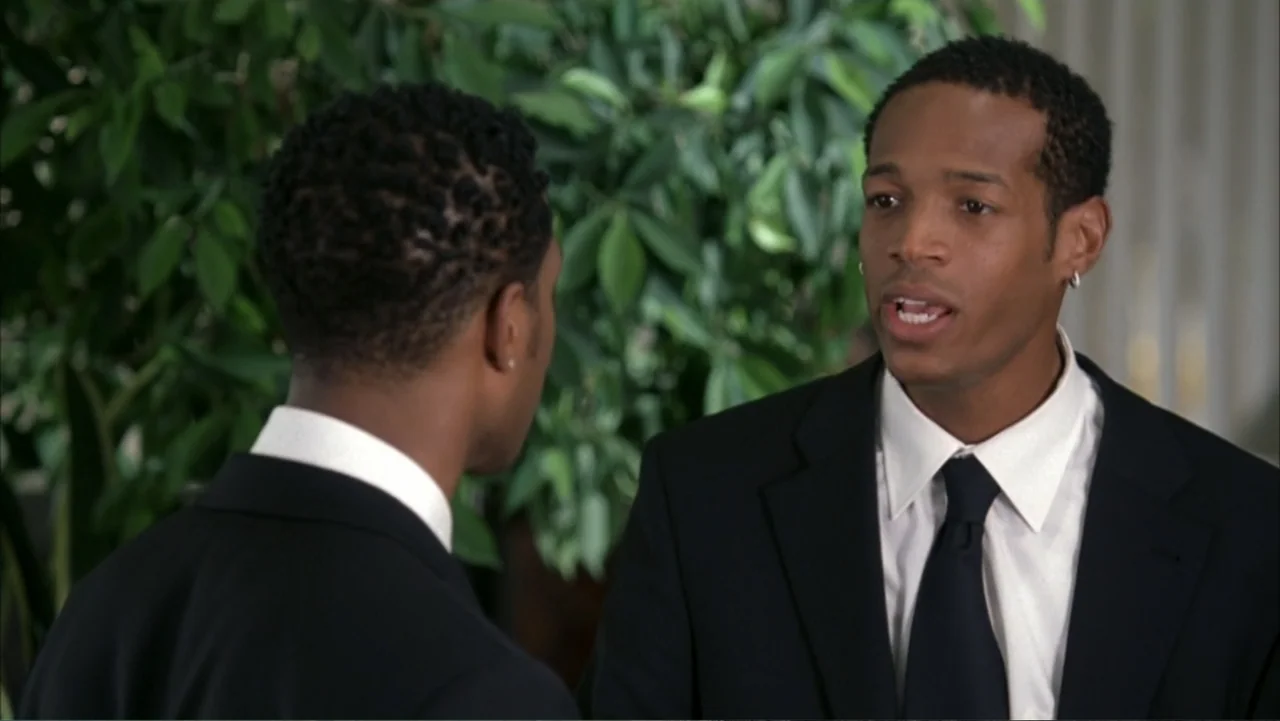White Chicks (2004) movie still: medium — Two men in professional business suits stand inside an office near a leafy plant. One man faces the camera…