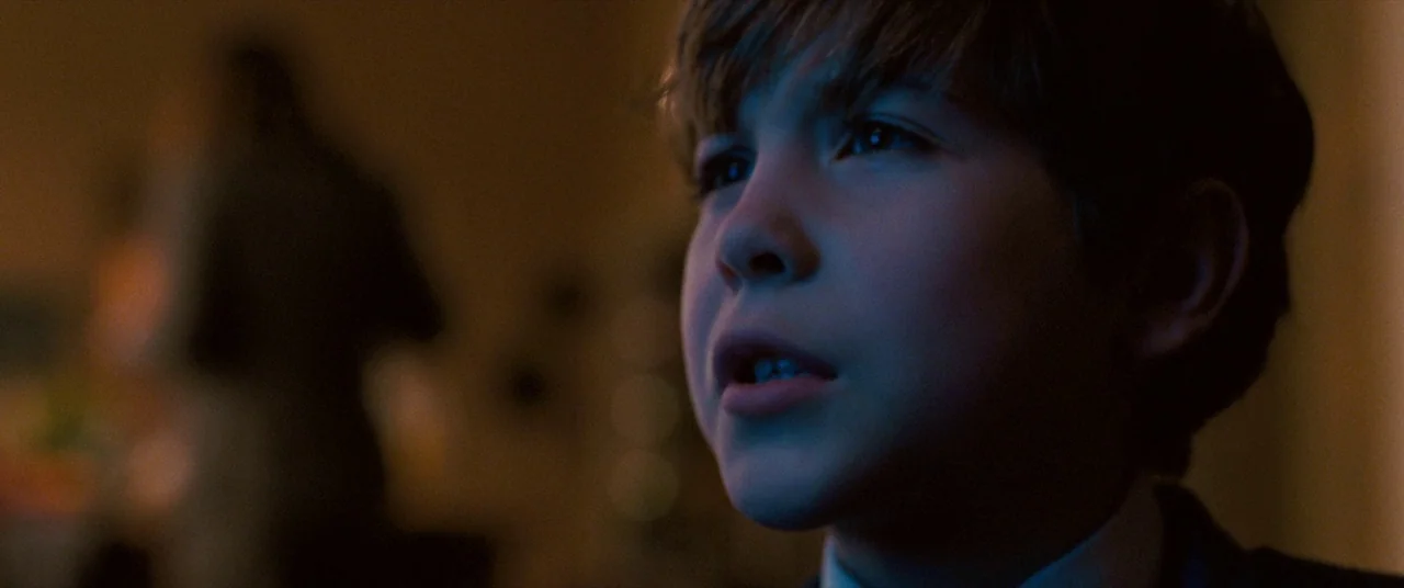 The Death and Life of John F. Donovan (2018) movie still: closeup — A dimly lit indoor space with the boy's face illuminated by artificial light. He…