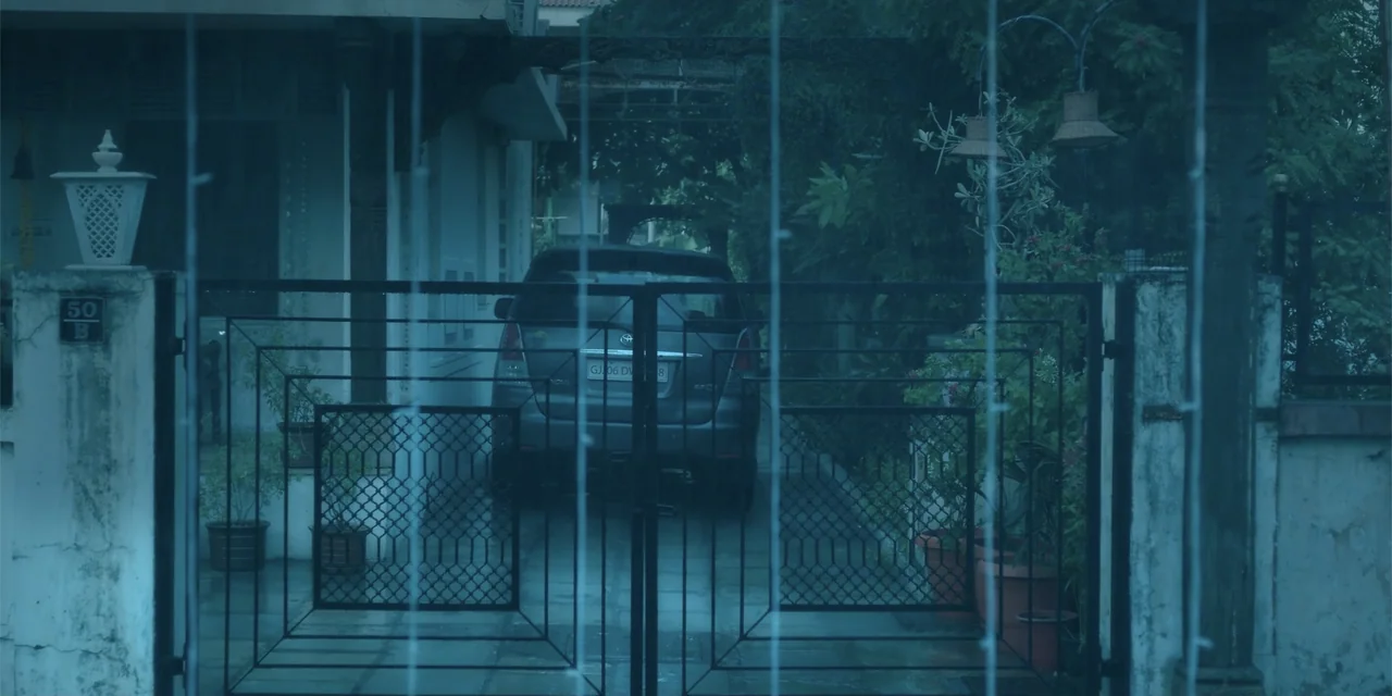 Maja Stoneface (1996) movie still: wide — A residential driveway is viewed through a closed black iron gate at night. An SUV sits parked in the…