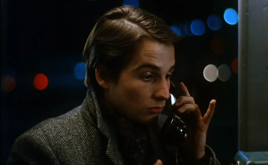 Stolen Kisses (1968) movie still: closeup — A man stands inside a telephone booth during the night. He holds a black handset to his ear while…