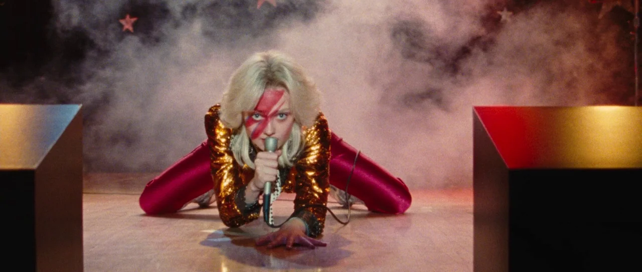 The Runaways (2010) movie still: fullbody — A dimly lit musical performance area with stars on the black backdrop. The performer kneels center frame…