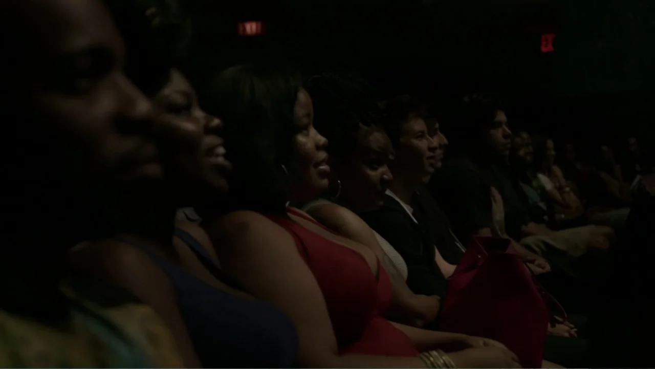 Mike Tyson: Undisputed Truth (2013) movie still: medium — A dark movie theater contains a group of people sitting in a row. They look forward toward…