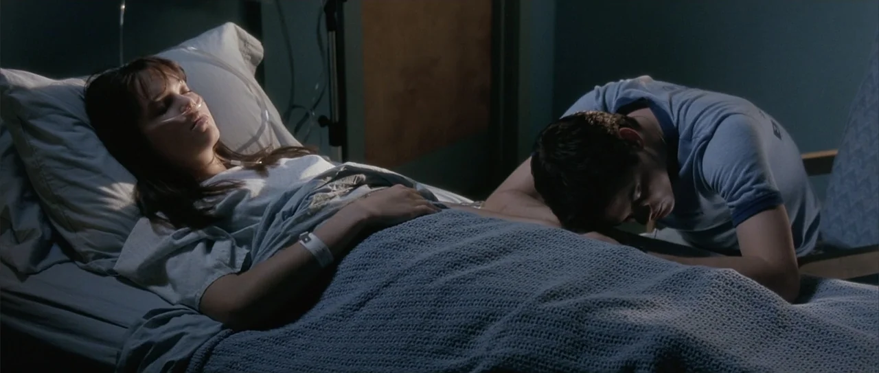 A Walk to Remember (2002) movie still: medium — A hospital room features a woman in a bed with medical equipment attached. A young man rests his…