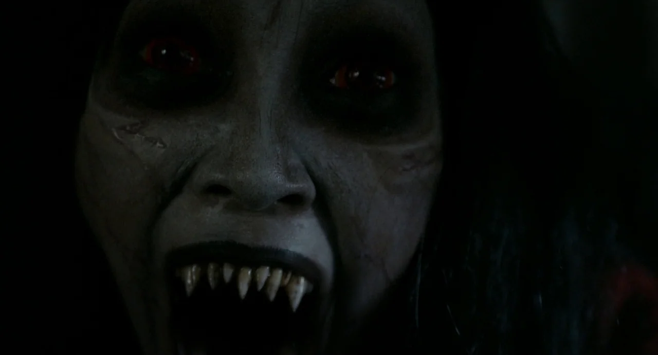 May The Devil Take You (2018) movie still: closeup — The face of a monstrous creature emerges from a pitch black surrounding environment. A…