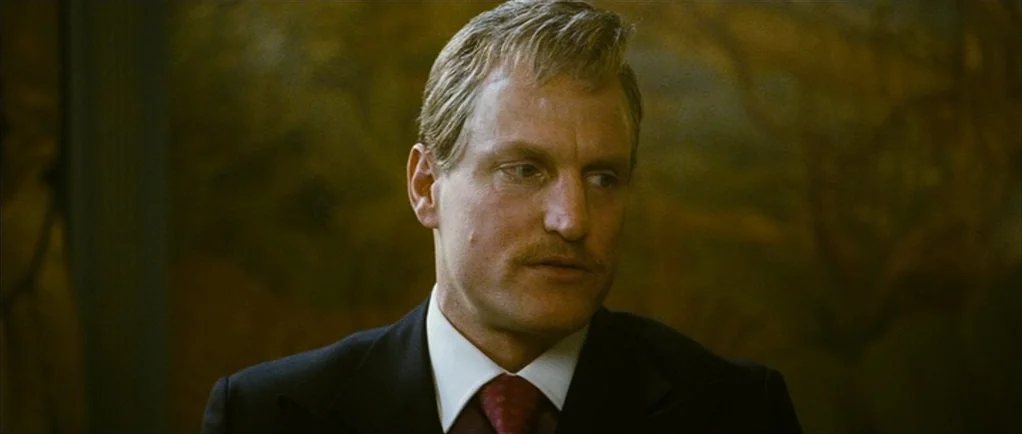 The Walker (2007) movie still: closeup — An interior space with a blurred dark textured wall in the background. A man in a dark suit sits while…
