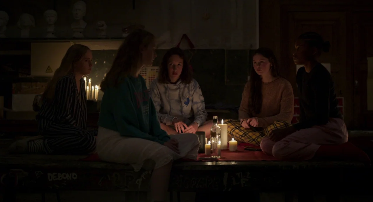 Zombi Child (2019) movie still: medium — A dark, cluttered art studio with plaster busts lining the high rear shelves. Five teenage girls sit…