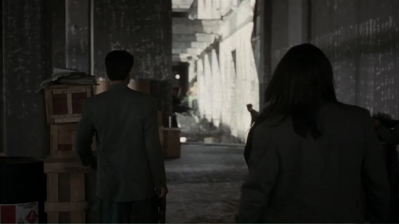 Behind Enemy Lines (2001) movie still: medium — A dark warehouse interior with large wooden crates stacked near the foreground wall. Two people…