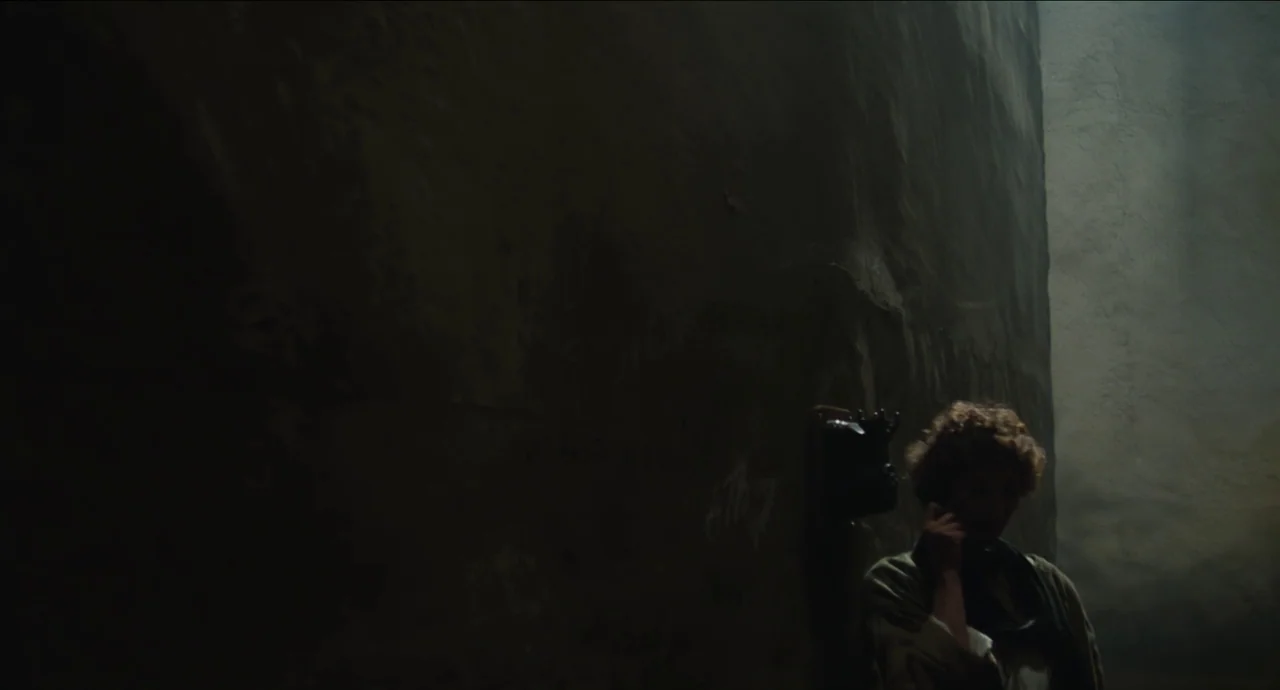 City of Women (1980) movie still: medium — A dimly lit concrete stairwell with a rough textured wall and visible graffiti. A woman with curly hair…