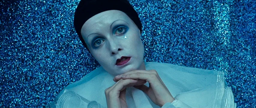 The Boy Friend (1971) movie still: closeup — A performer sits against a dense wall covered in sparkling blue sequin material. The individual wears…