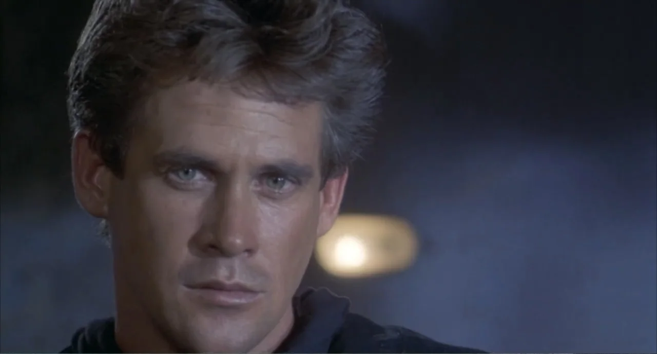 American Ninja 4: The Annihilation (1990) movie still: closeup — A dark indoor space with a blurred, out-of-focus light source behind the subject. A…
