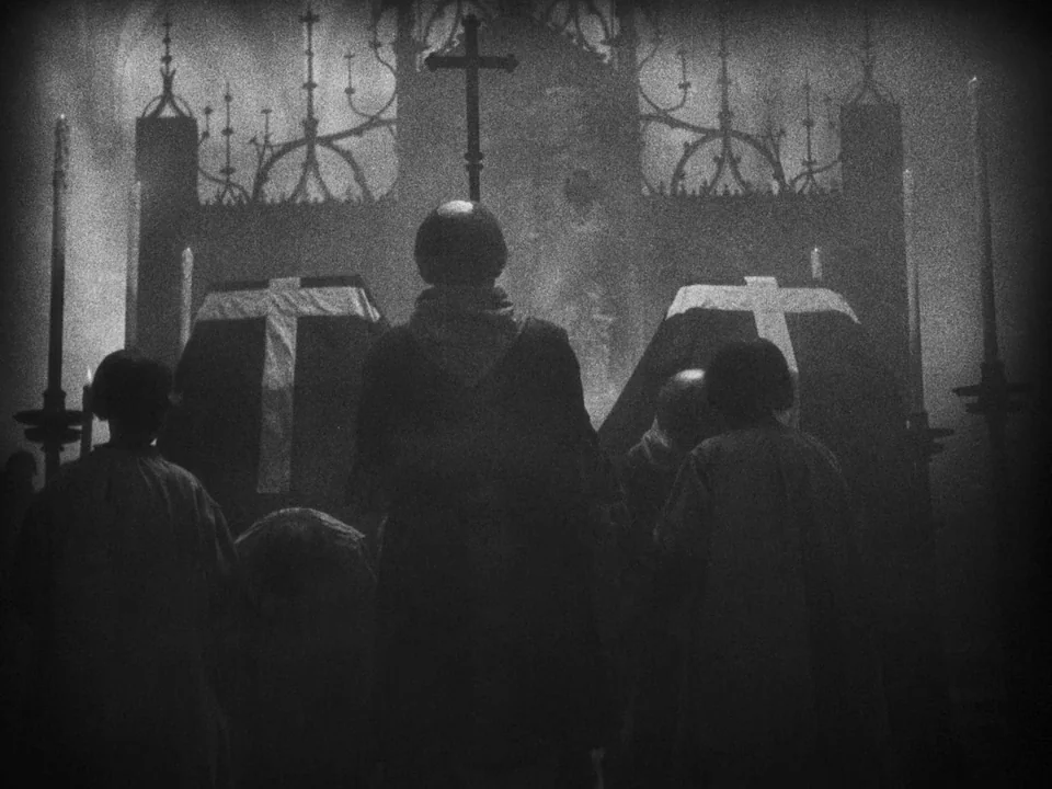 Faust (1926) movie still: medium — A dark stone interior features rows of figures standing before two coffins with crosses. The central figure faces…
