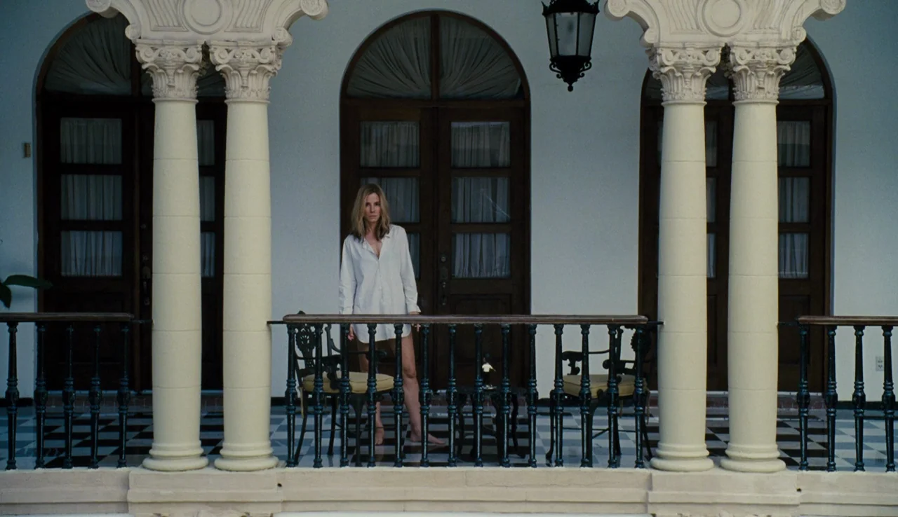 Our Brand is Crisis (2015) movie still: fullbody — A stone balcony features neoclassical columns and a black-and-white checkered tile floor. A woman…