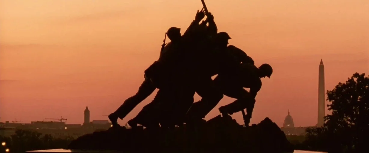 Independence Day (1996) movie still: fullbody — The Marine Corps War Memorial stands as a dark silhouette against a sunset sky. Multiple bronze…