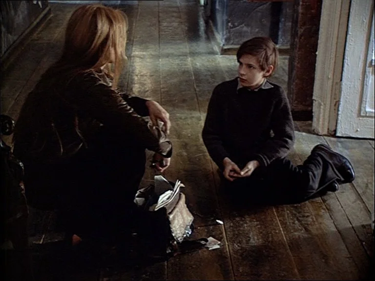 Mirror (Зеркало, Zerkalo) (1975) movie still: medium — A wooden hallway with worn floorboards features a woman and child sitting down. The pair sit…