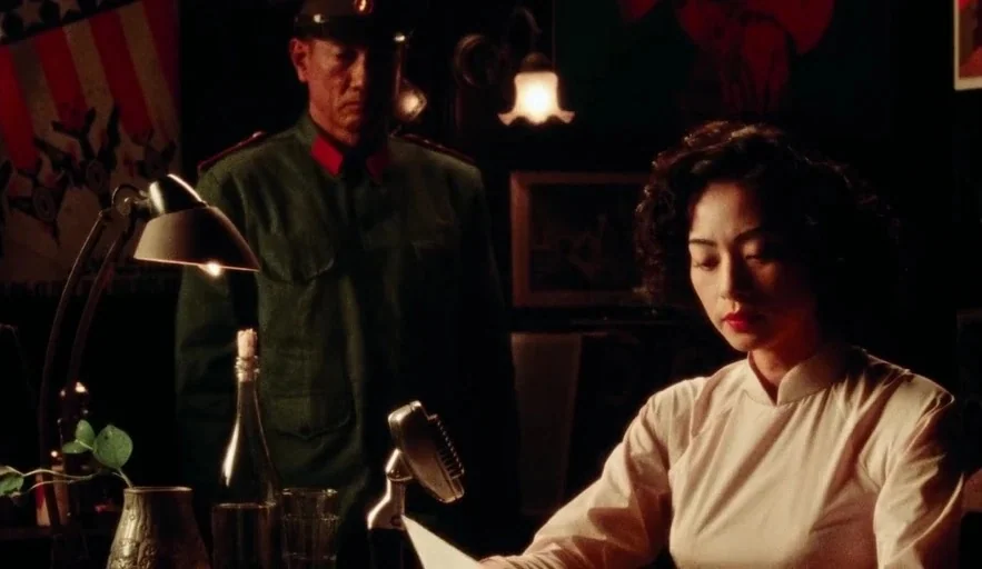 Da 5 Bloods (2020) movie still: medium — A dimly lit room contains a microphone and a desk lamp on a surface. A woman reads a document while an…