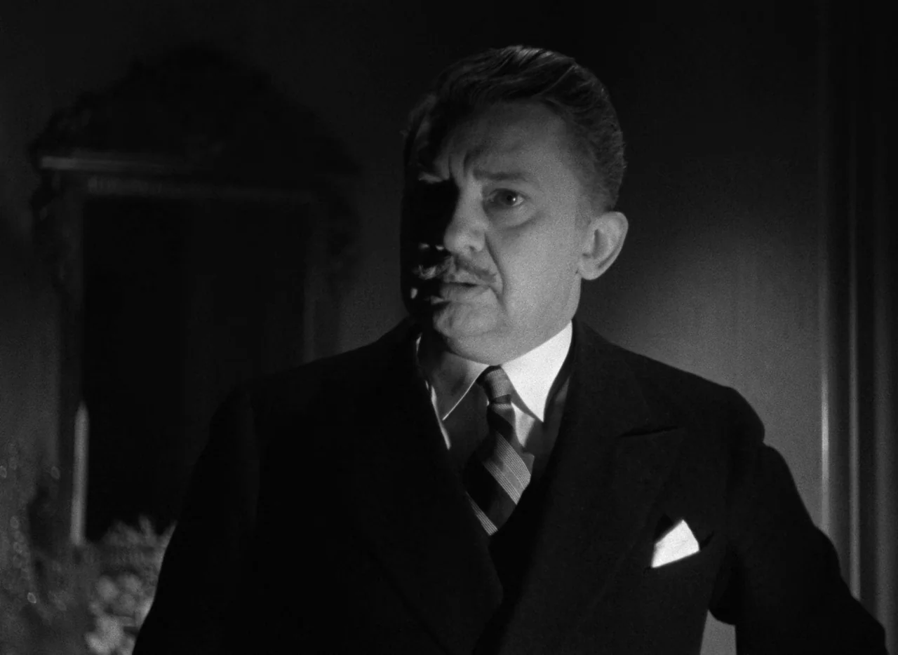Mark of the Vampire (1935) movie still: medium — An interior space features deep shadows obscuring the background furniture and details. A man in a…