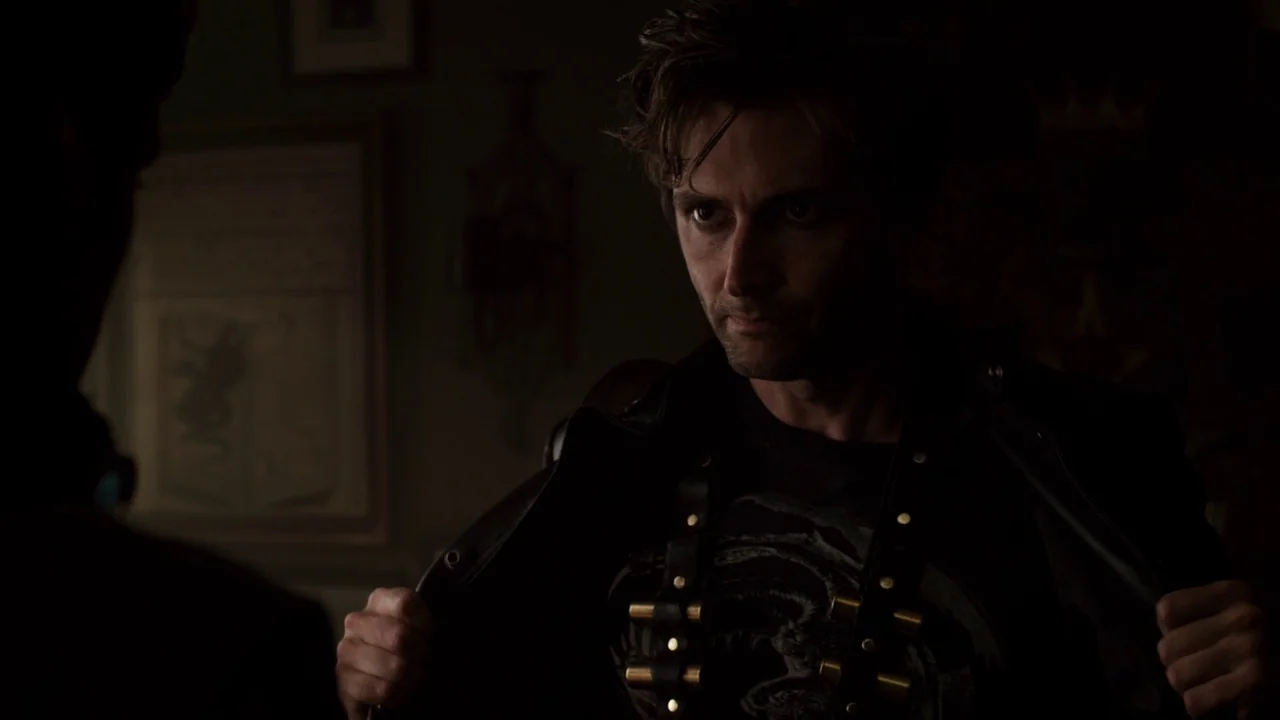 Fright Night (2011) movie still: medium — A dimly lit room with framed artwork visible on the dark wall behind the subject. A man adjusts the edges…