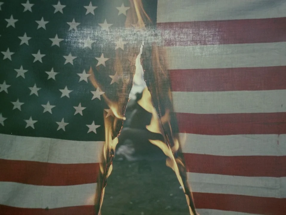 Throw Away Your Books, Rally in the Streets (1971) movie still: closeup — A fabric American flag is held taut while a vertical tear burns down the…