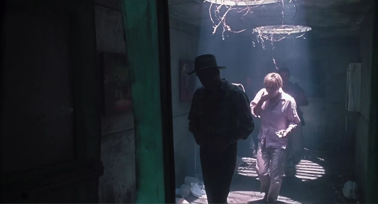 Jurassic Park III (2001) movie still: medium — A dimly lit narrow space features a grate above emitting a strong light beam. A man wearing a hat and…