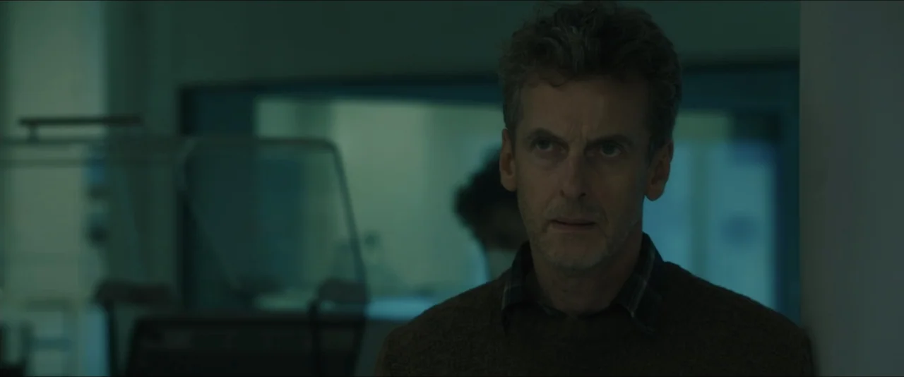World War Z (2013) movie still: medium — A sterile room with a large glass window separating a background work area. A middle-aged man in a brown…