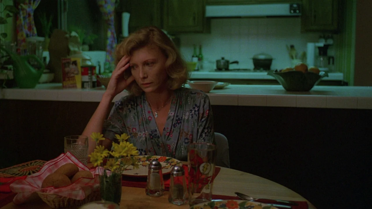 Paris, Texas (1984) movie still: medium — A suburban home features a muted color palette with retro 1980s wooden cabinetry. A woman sits alone at a…