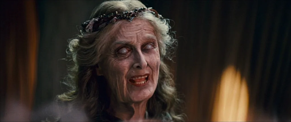 Your Highness (2011) movie still: closeup — An elderly woman stands in a dim, shadowed indoor space with dark drapery. Her eyes are entirely white…
