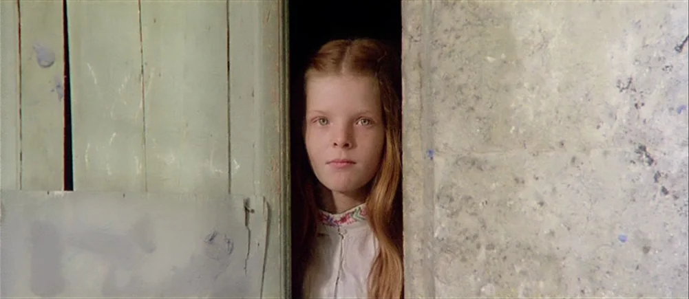 Deep Red (1975) movie still: closeup — A young girl with long auburn hair stands in a narrow dark doorway. She gazes forward while framed between a…