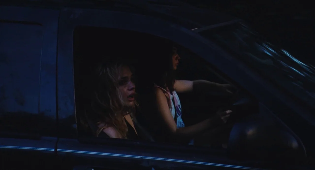 The Giant (2019) movie still: medium — The interior of a dark car at night with two women present. One woman looks out the passenger window while…