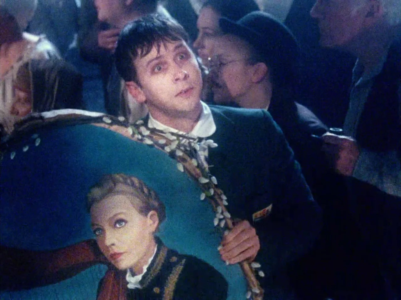 The Twentieth Century (2019) movie still: medium — A dimly lit, crowded gathering features people in dark clothing pressed close together. A young…