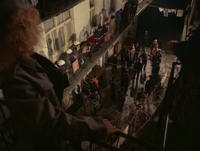 WR: Mysteries of the Organism (1971) movie still: wide — A multi-story tenement building with metal balconies overlooks an enclosed paved courtyard…