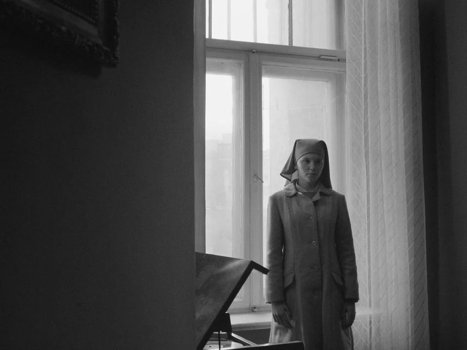 Ida (2013) movie still: medium — A plain interior room features a tall white window with translucent curtains. A woman wearing a religious habit…
