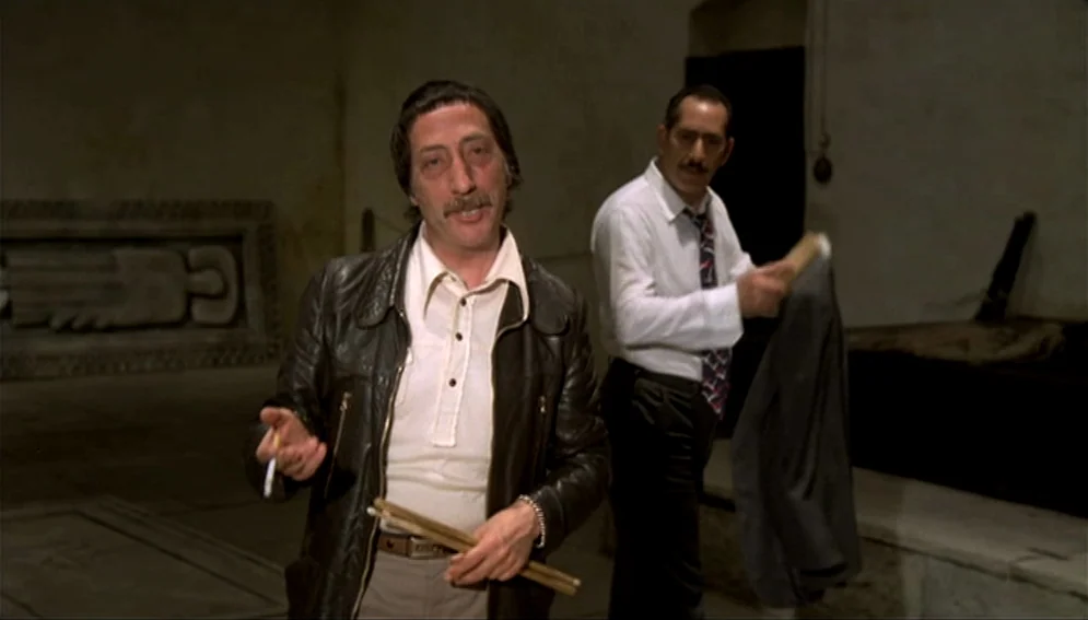 Orchestra Rehearsal (1978) movie still: medium — A stone-walled underground space features carved tomb markers and low-ceilinged architectural…