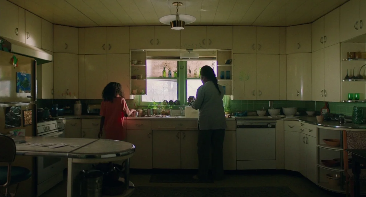 Fast Color (2018) movie still: wide — A home kitchen with wood cabinets, light green backsplash tile, and a central window. A child and an older…