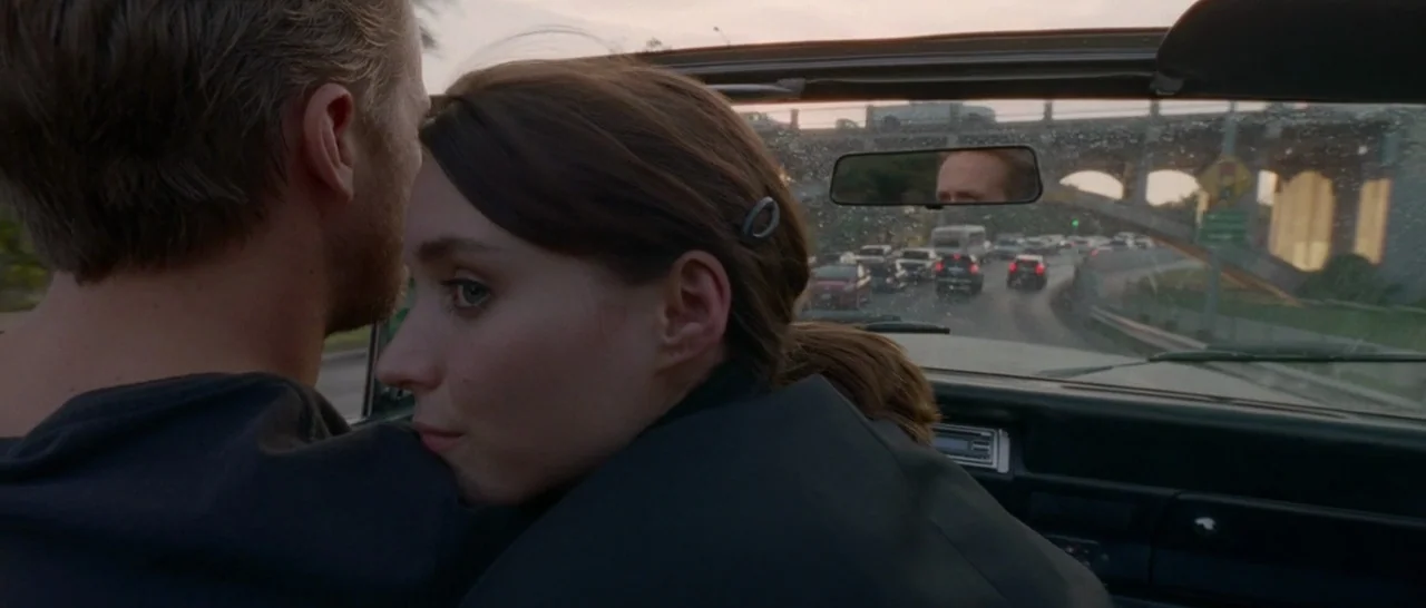 Song to Song (2017) movie still: medium — A woman leans her head against a man's shoulder inside a moving car. Traffic is visible through the front…